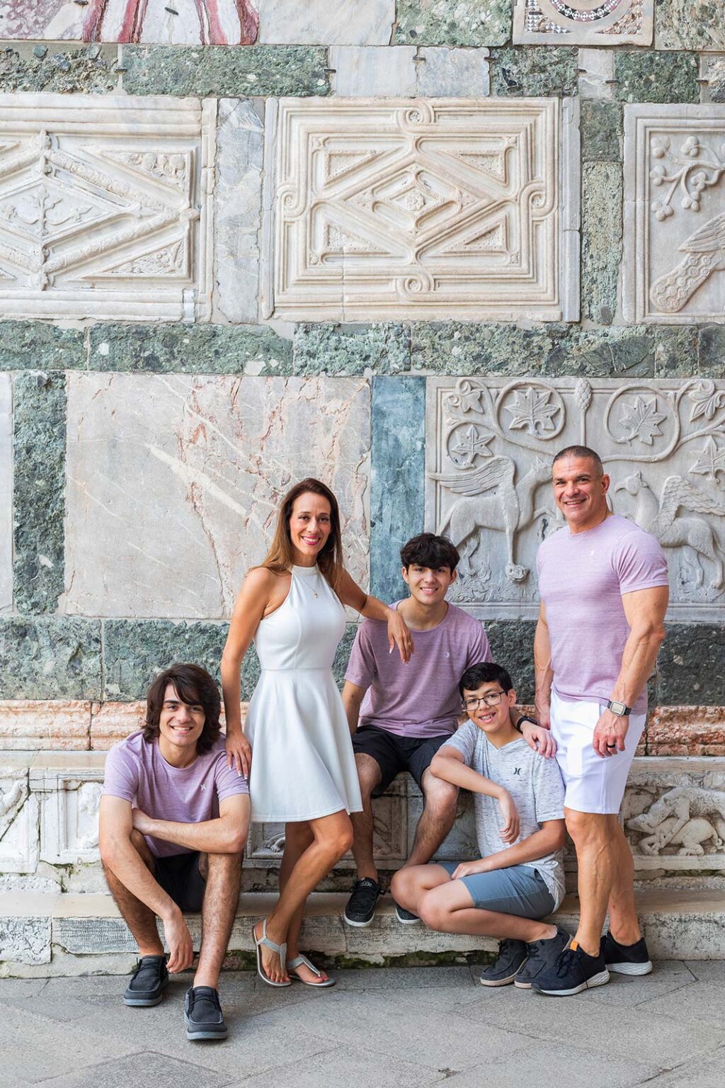 Parents and their three teenage sons sitting on the marble bench along St Mark&rsquo;s Basilica, Venice