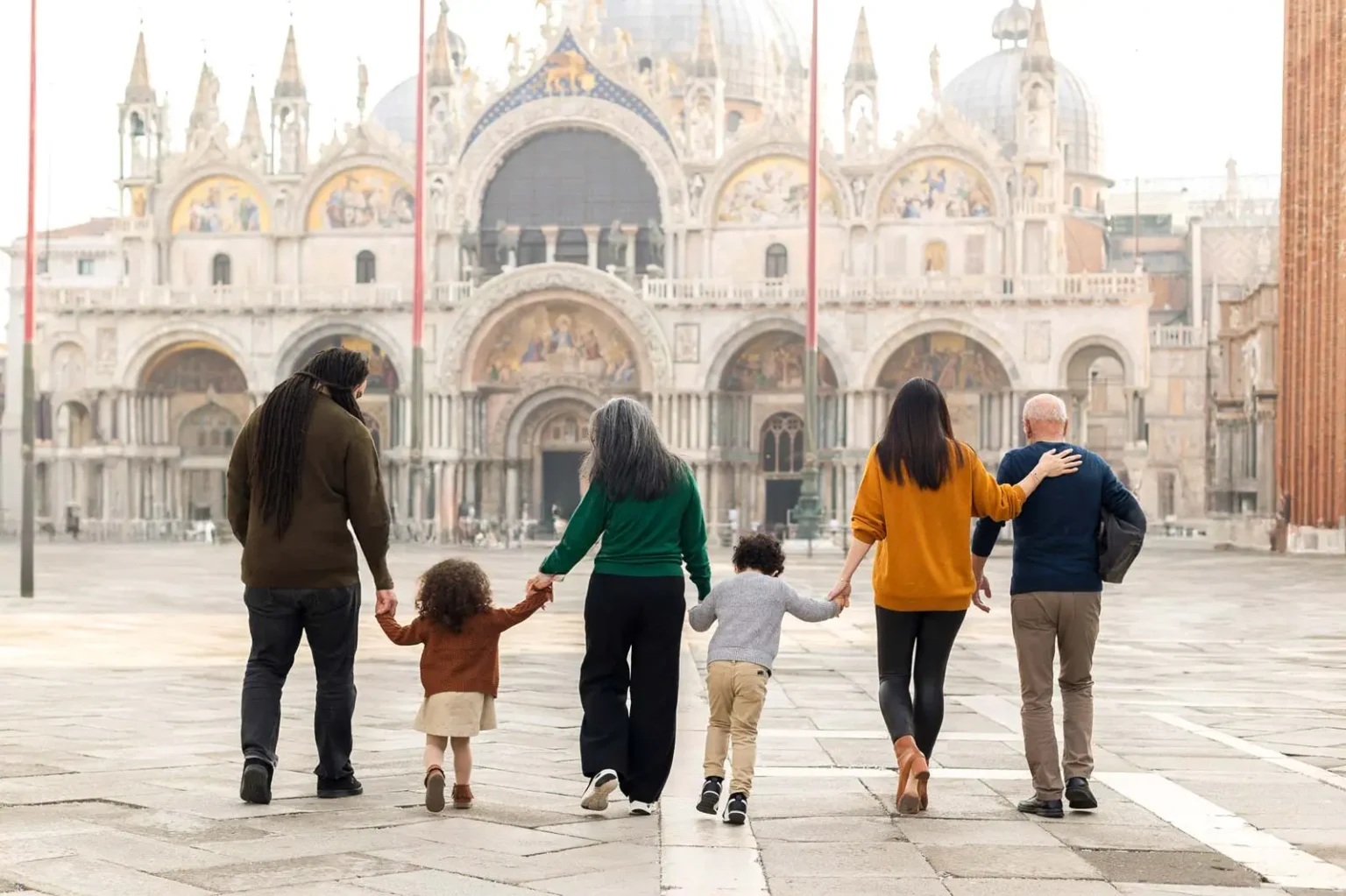 A family with two small children walking hand in hand across an empty St Mark&rsquo;s Square in the early morning, Venice