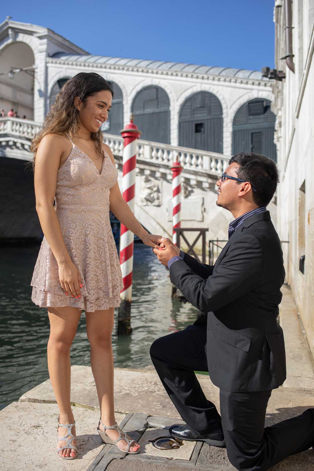 Man proposing to his partner near Rialto Bridge in Venice, holding hands on a sunny day