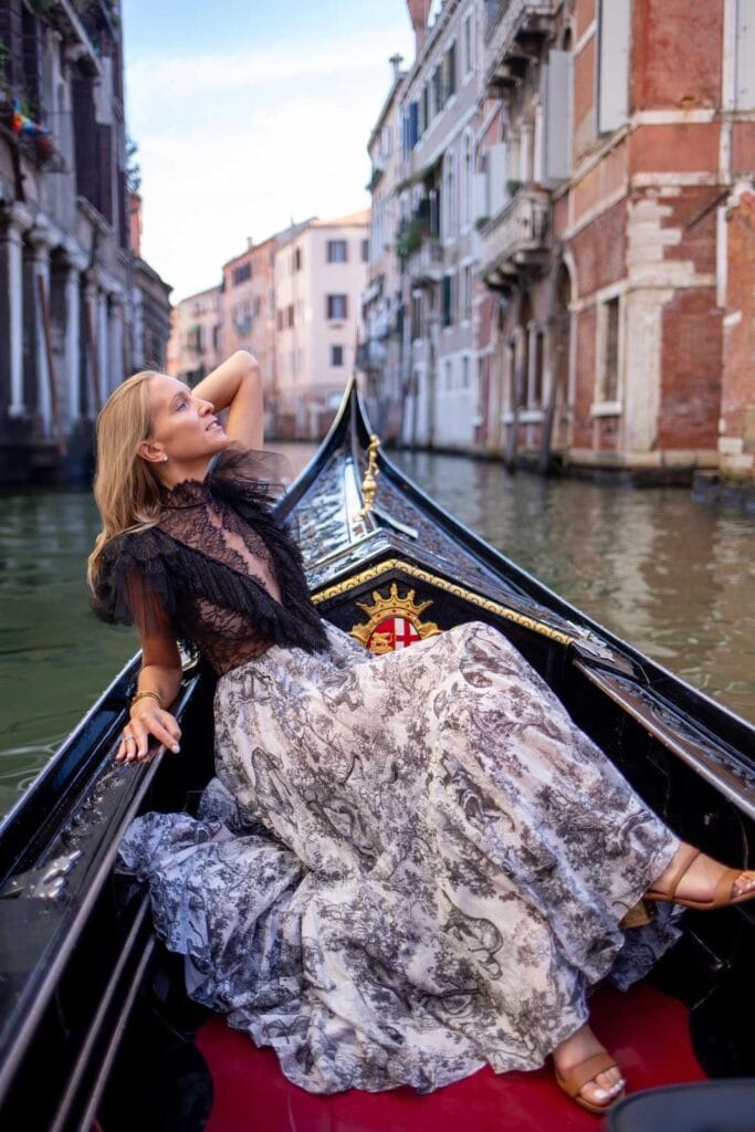 Woman reclining across a gondola as it glides through a quiet inner canal in Venice