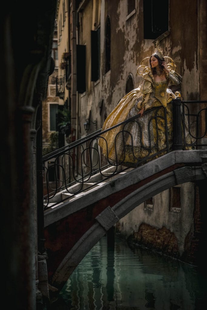 Woman lifting the hem of a long dress while walking up the stone steps of a Venetian bridge