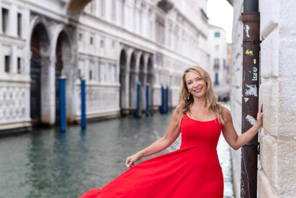 Woman in a red dress standing in front of the pale marble arcades of St Mark’s Square