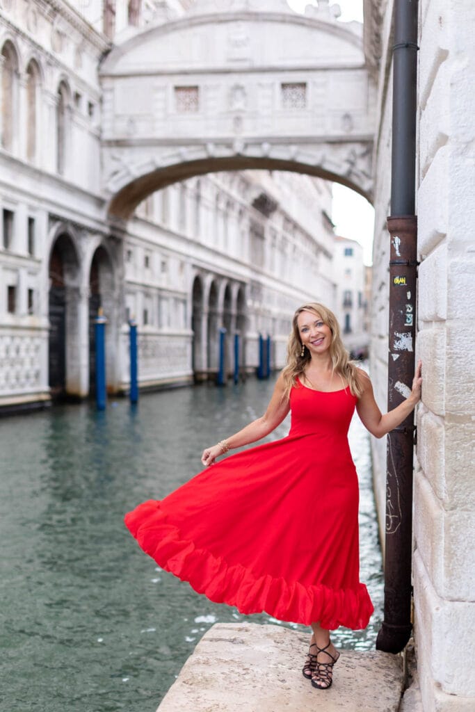 Woman in a red dress standing in front of the pale marble arcades of St Mark’s Square