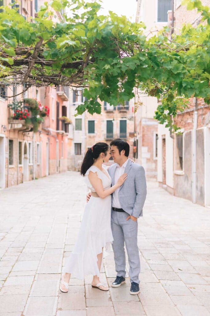 Couple in beige and light blue standing against a brick wall in a quiet Venetian street